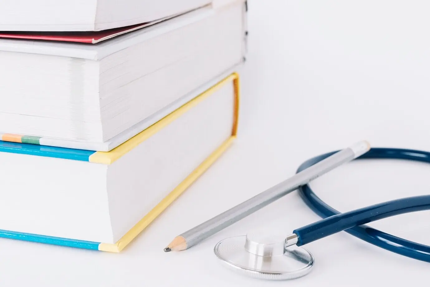 Libros apilados; lápiz y estetoscopio sobre una superficie blanca.